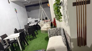 Una mesa de billar, un sofá estampado con diseño de cebra y un sillón colgante blanco en una habitación con suelo de césped artificial.