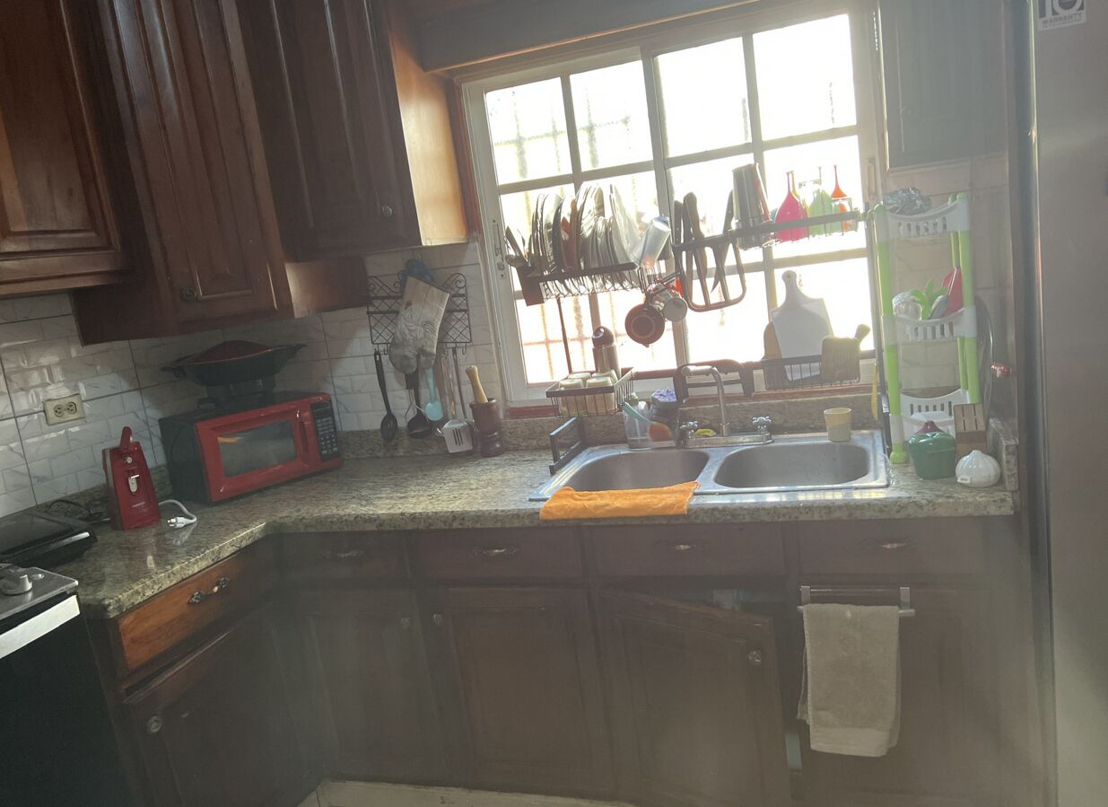 A kitchen with wooden cabinets, a granite countertop, a microwave, a sink, and a window with a view of the outside.