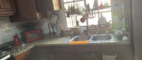 A kitchen with wooden cabinets, a granite countertop, a microwave, a sink, and a window with a view of the outside.