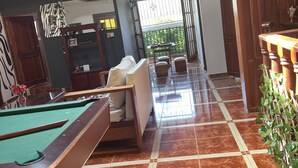 Una mesa de billar en una habitación amplia con techo alto y vistas al exterior.