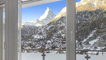 Blick aus dem Fenster auf ein Bergdorf mit schneebedeckten Häusern und einem markanten Berggipfel.