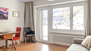 Ein Zimmer mit Holztisch, zwei Stühlen, einer Couch und einem großen Fenster mit Bergblick.