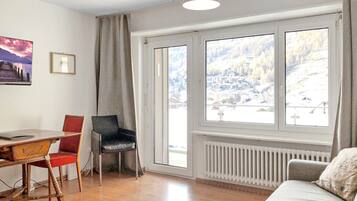 Ein Zimmer mit Holztisch, zwei Stühlen, einer Couch und einem großen Fenster mit Bergblick.