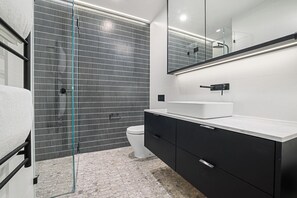 Un baño moderno con cabina de ducha de vidrio, inodoro blanco y tocador negro con encimera blanca.
