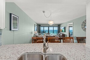 A kitchen with granite countertops, a double sink, and a dining area with a view of the ocean.