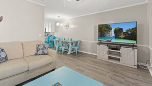 A living room with a sofa, a coffee table, a TV, and a dining area with chairs and a table. - Absolute Beach ~ Pet-Friendly Townhome with Private Backyard (Panama City Beach)