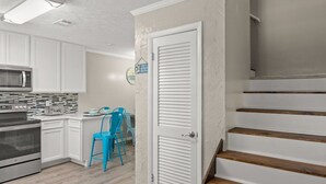 A kitchen with white cabinets, a microwave, and a toaster. There is a blue chair and a staircase with wooden steps. - Absolute Beach ~ Pet-Friendly Townhome with Private Backyard (Panama City Beach)