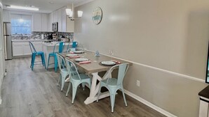 A modern kitchen with white cabinets, a wooden dining table, and blue chairs. - Absolute Beach ~ Pet-Friendly Townhome with Private Backyard (Panama City Beach)