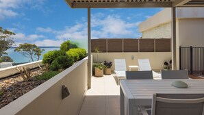Une terrasse extérieure couverte avec vue sur la mer, une table avec des chaises et des plantes en pot.