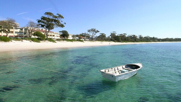Un bateau amarré  à un quai, sur une plage de sable fin, avec des bâtiments en arrière-plan.