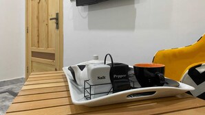 A wooden table with a tray containing salt and pepper shakers, a black mug, and a white mug. A television with a red 'N' logo is mounted on the wall above the table. - Dastak Hotels  (Islamabad)