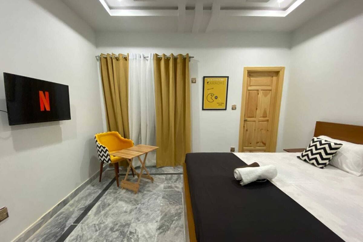A hotel room with a bed, a TV mounted on the wall, a small table, and a chair.