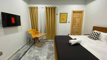 A hotel room with a bed, a TV mounted on the wall, a small table, and a chair.