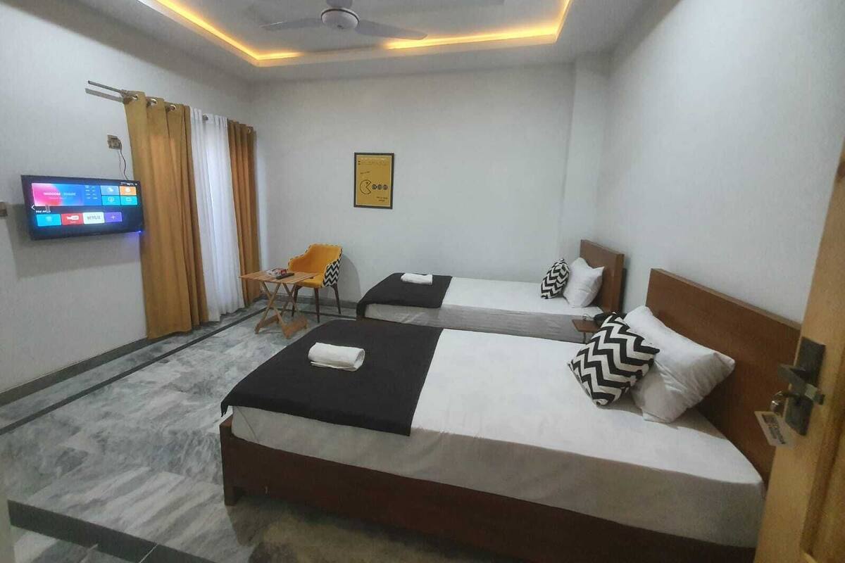 A hotel room with two beds, a flat-screen TV mounted on the wall, a ceiling fan, and a small table with a chair.