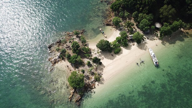 Vue aérienne d’une plage aux eaux turquoise et limpides, bordée de formations rocheuses et d’une végétation luxuriante.