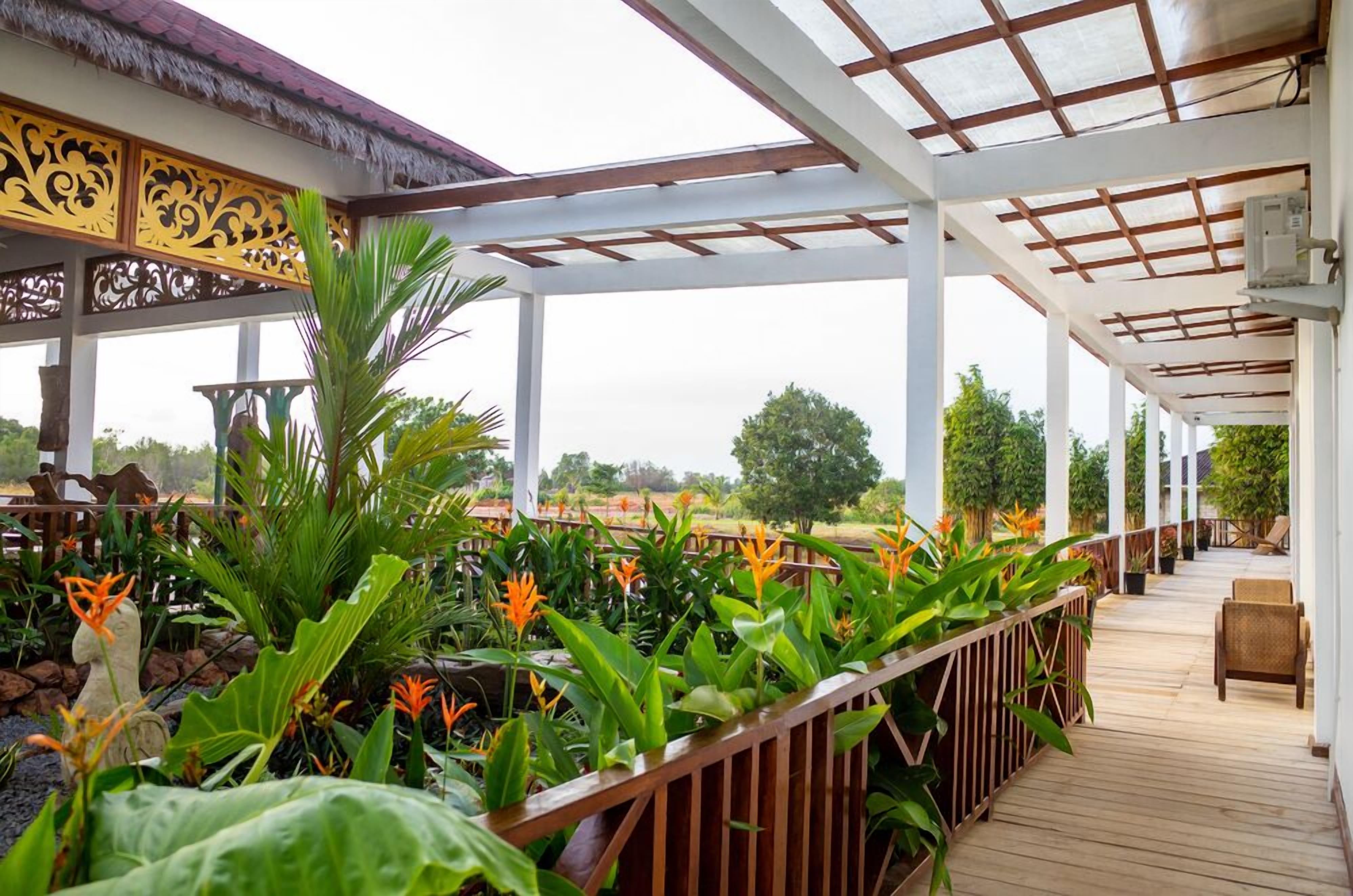 A covered outdoor area with a wooden deck, surrounded by lush tropical plants and a thatched roof structure.