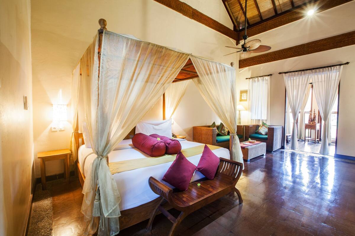 A room with a four-poster bed, a wooden bench, and a ceiling fan.