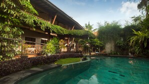 A pool area with a clear blue pool, surrounded by lush greenery and a building with a covered patio. - Dwaraloka Retreat Ubud (Ubud)