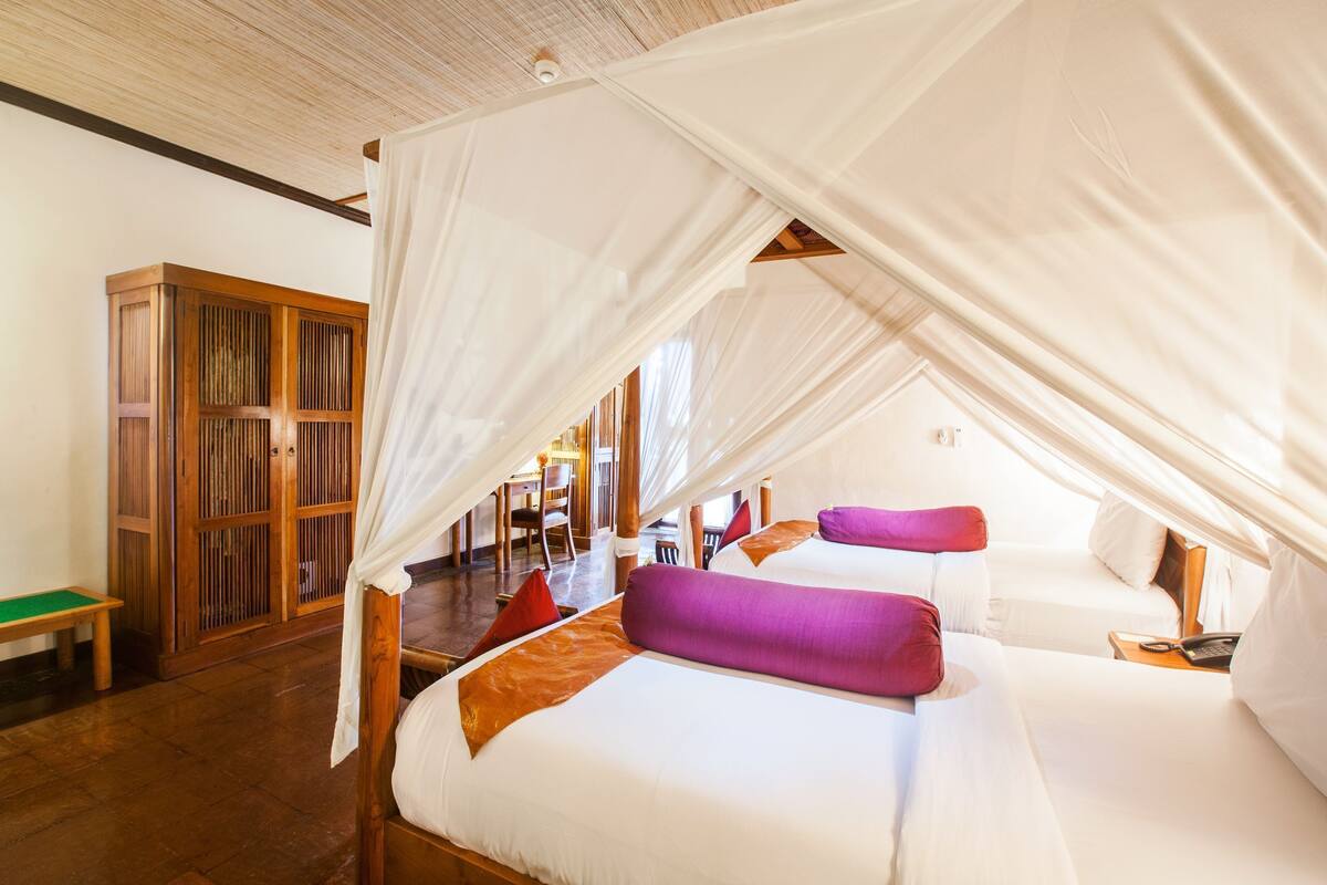 A room with two beds, a wooden cabinet, and a bench.