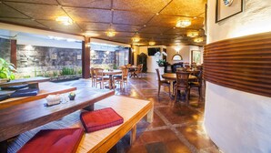 A restaurant with wooden tables and benches, stone walls, and a tiled floor. - Dwaraloka Retreat Ubud (Ubud)