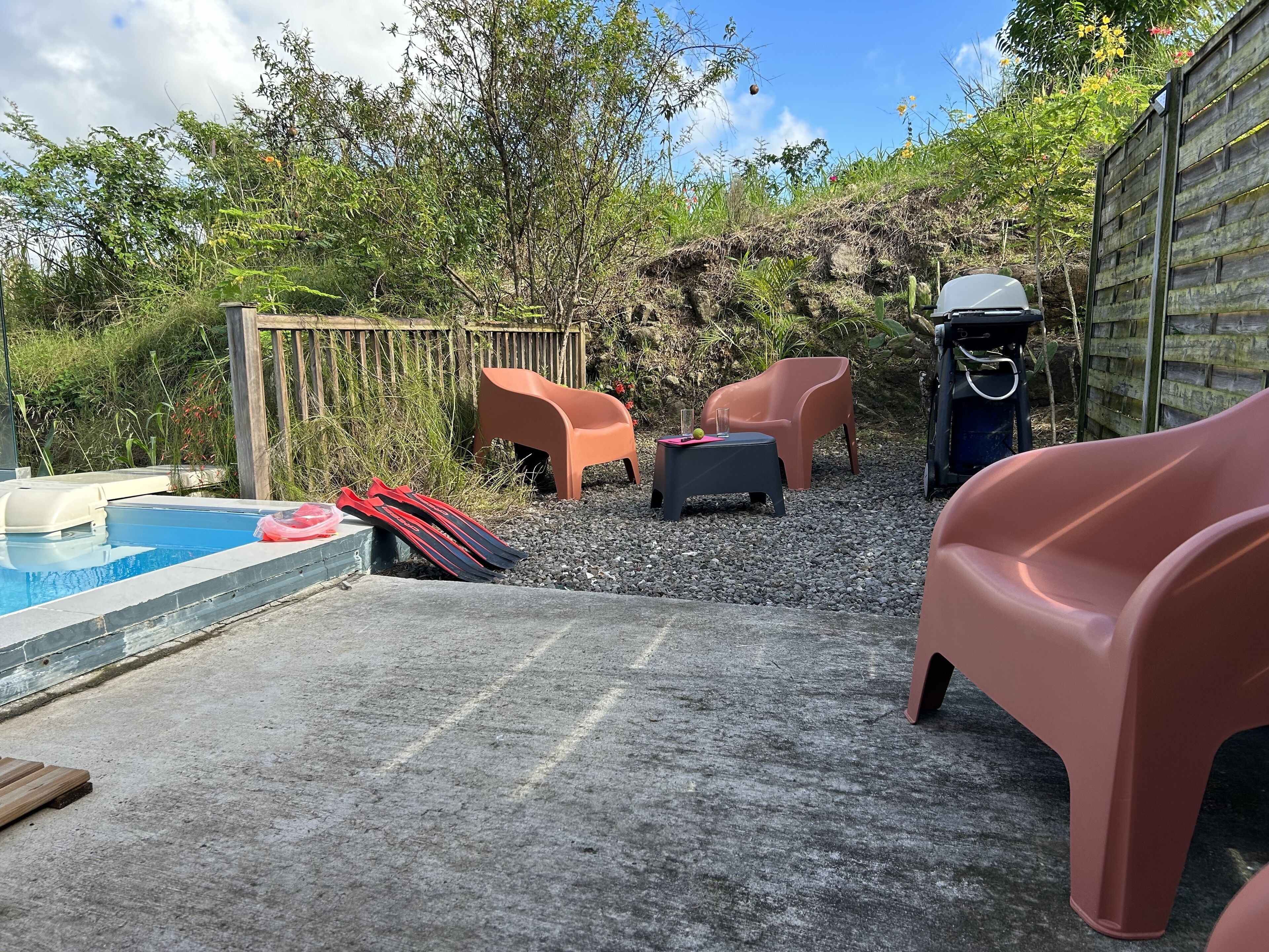 A pool area with a hot tub, two chairs, and a table with a drink.
