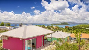 A pink house with a large open patio, a swimming pool, and a view of a lake and mountains. - Villa Jalna grenadine with private pool in Martinique (Trois-Ilets)