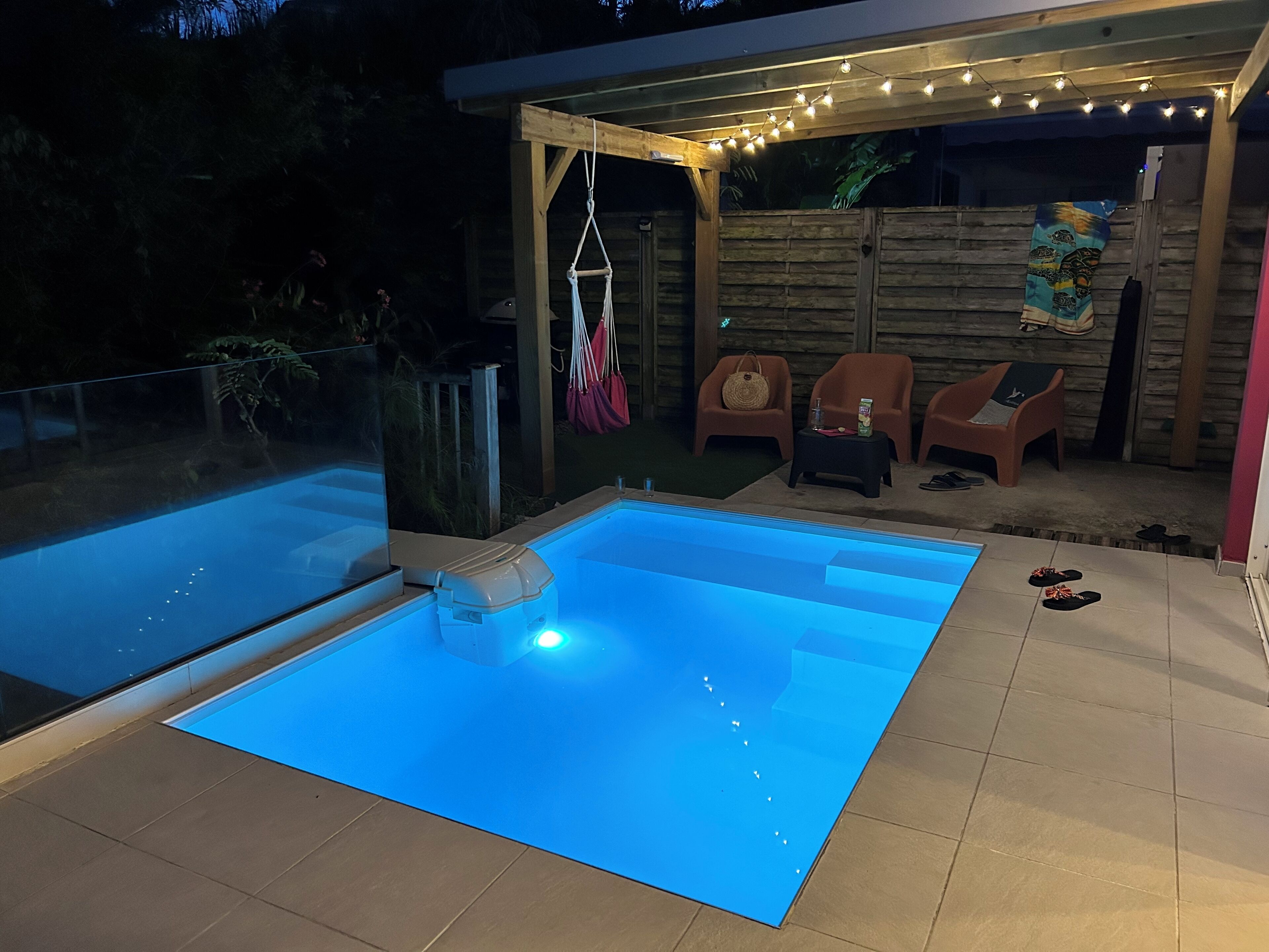 Ein Schwimmbad mit Glasüberdachung, umgeben von einer Terrasse mit Stühlen und einem Tisch.