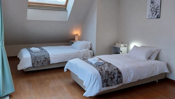 A room with two beds, a skylight, a painting, and a bedside table with a lamp. - Miyuki Townhouse (Furano)