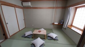 A traditional Japanese room with tatami flooring, a low wooden table, cushions, a shelf with items, and a window with curtains. - Miyuki Townhouse (Furano)
