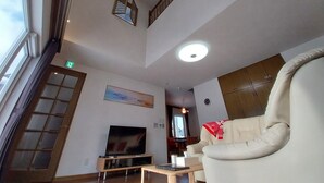 A high-ceiling living room with a television, sofa, and a painting. - Miyuki Townhouse (Furano)