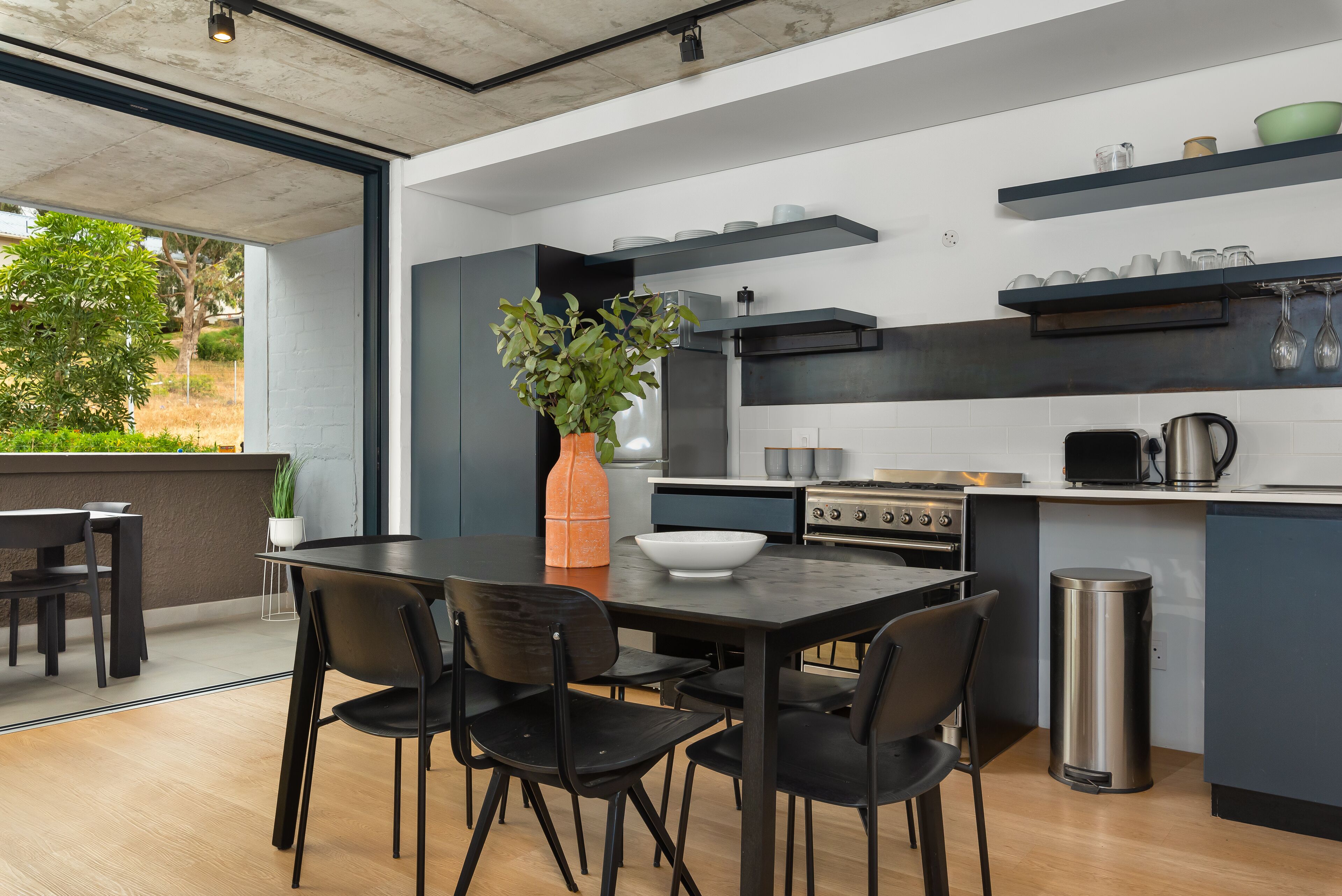A modern kitchen with a dining area, featuring a large table, chairs, and a potted plant.
