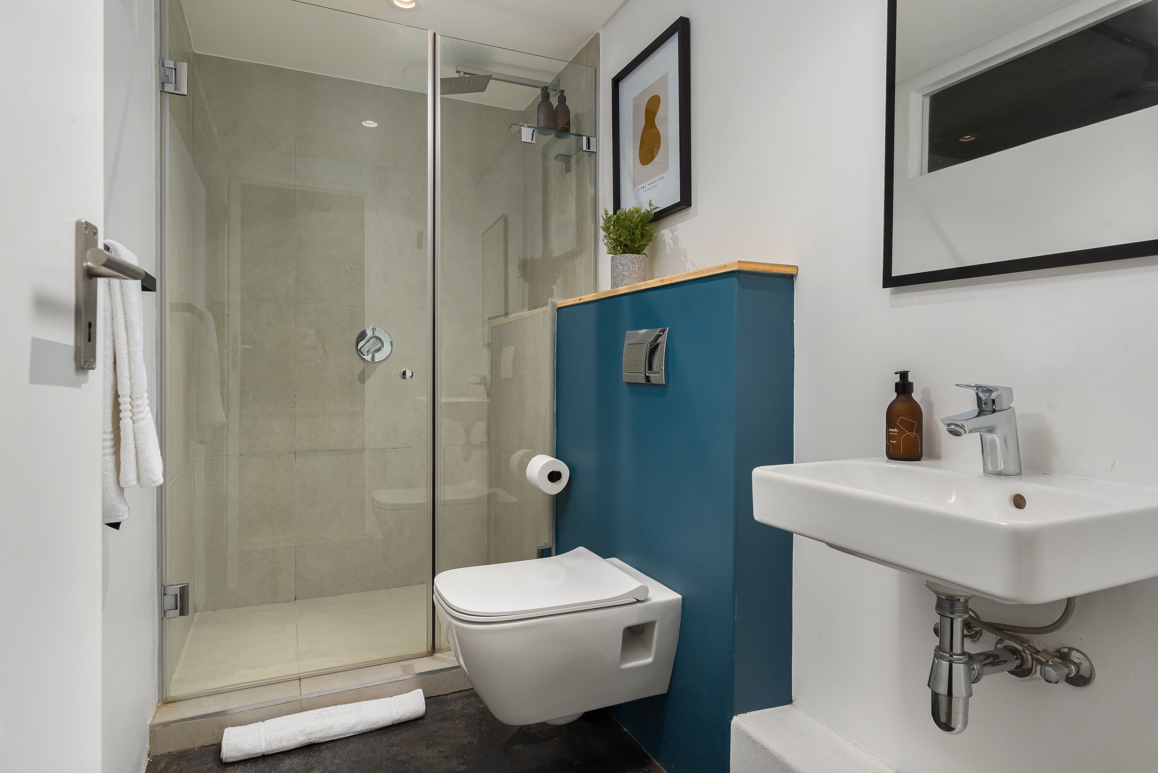 Une salle de bain moderne avec une douche à parois de verre, des toilettes blanches, un lavabo et un tableau encadré au mur.