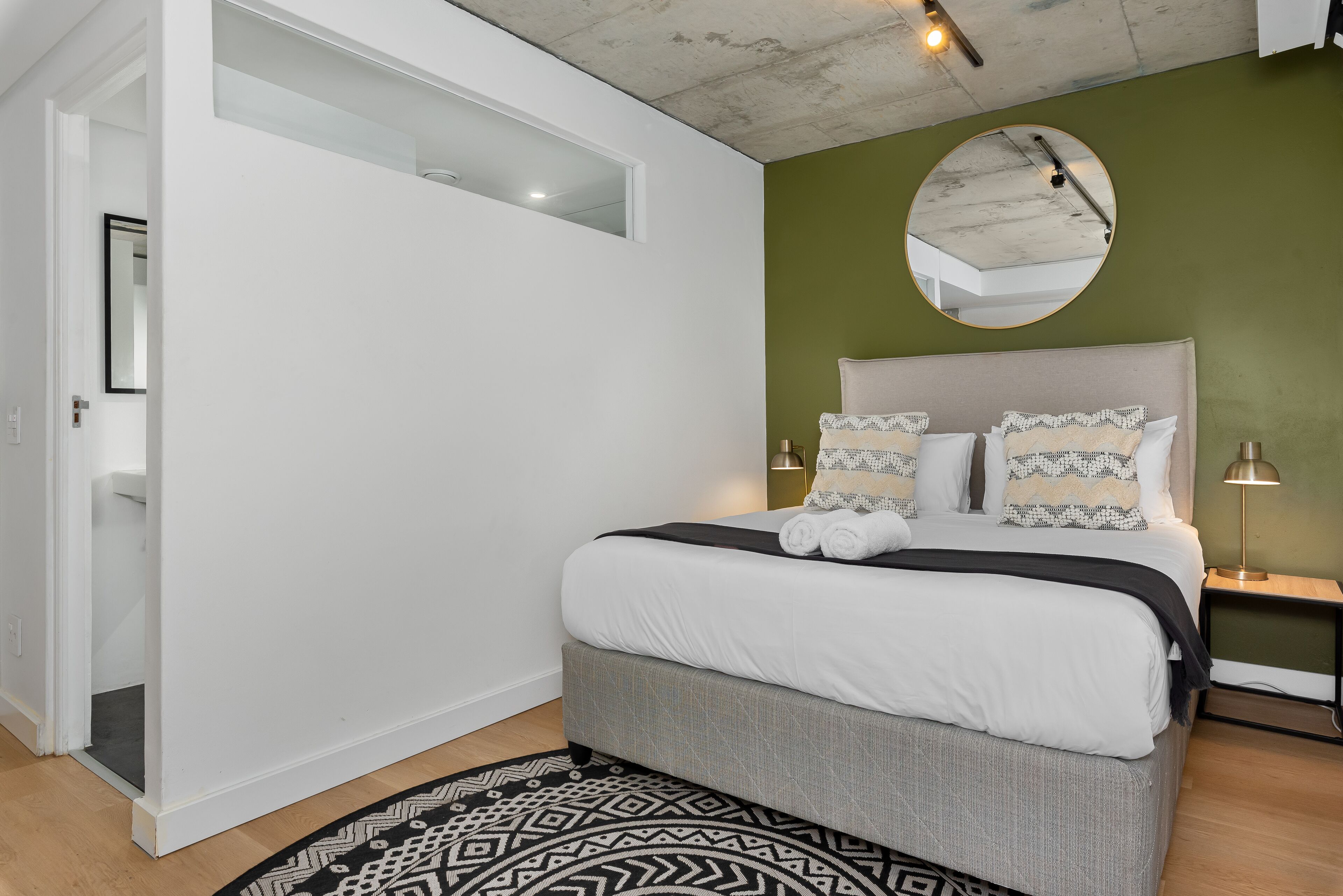 A bedroom with a bed, a round mirror, and a nightstand.