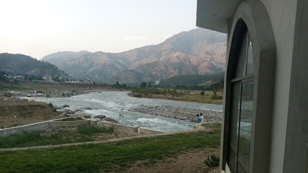 Un fiume con un letto roccioso, circondato da colline e alcuni edifici in lontananza.