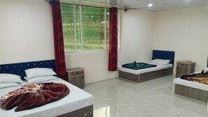 Una camera d'albergo con due letti, una finestra con tende, un pavimento piastrellato e un piccolo tavolo.