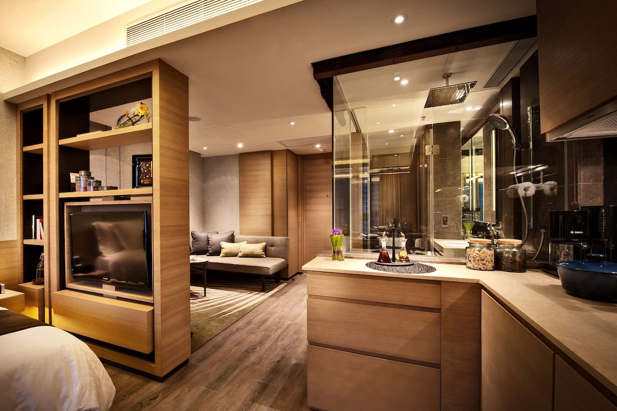 A modern hotel room with a large wardrobe, a sofa, a dining area, and a kitchen.