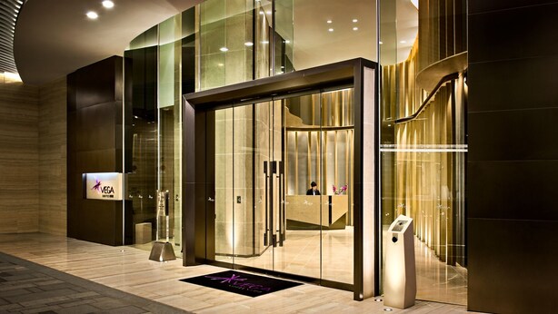 A modern hotel entrance with a glass door, a digital signboard, and a reception desk. - Vega Suites (Sai Kung)