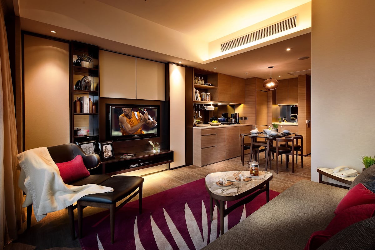 A modern living room with a flat-screen TV, a dining area, and a kitchenette.