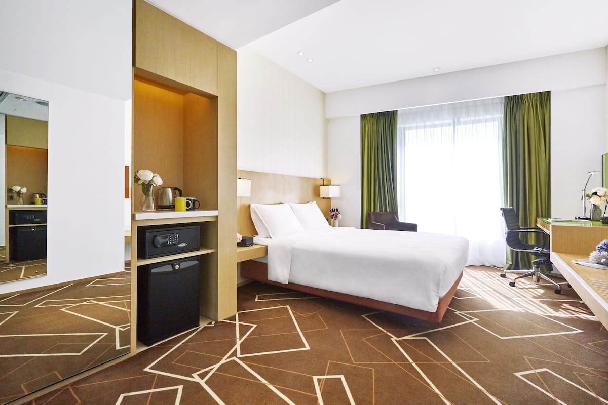 A hotel room with a bed, desk, chair, and a small kitchenette.