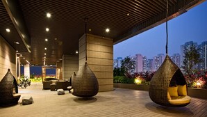 A modern outdoor seating area with hanging chairs and a cityscape view in the background. - Vega Suites (Sai Kung)