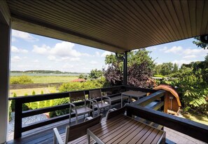 Un espacio al aire libre techado con un deck de madera, asientos y vistas a un lago y follaje.