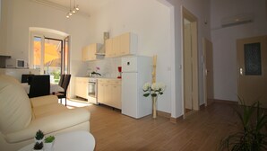 Un salon moderne comprenant un canapé, une table basse et un petit coin cuisine avec un réfrigérateur, une cuisinière et des placards.