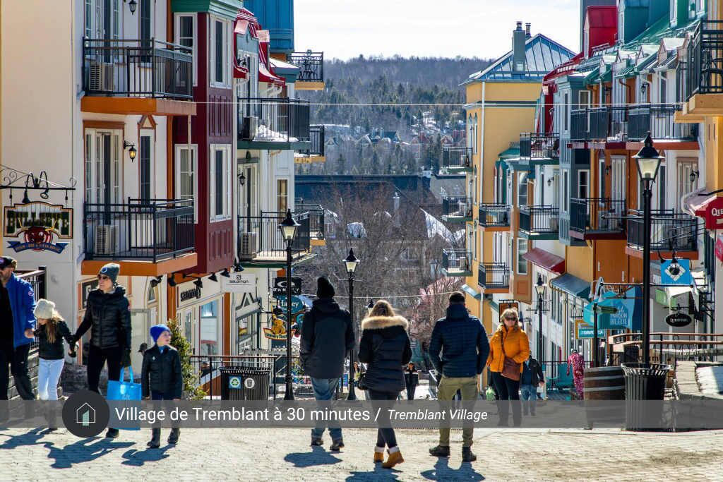 A colorful street with people walking, a sign for Tremblant Village, and a view of a hill in the background.