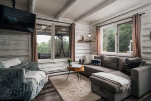 A cozy cabin interior with a sofa, a chair, a coffee table, and a TV mounted on the wall. - Lakefront Chalet w/ Hot Tub & Kayaks, Near Tremblant (Lac-Supérieur)