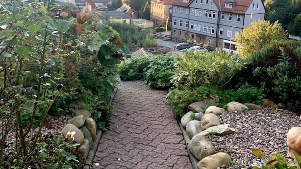 A pathway leading to a multi-story building surrounded by lush greenery and hills. - Vacation apartment on a hillside with a picturesque view (Osterode am Harz)