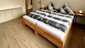 A bedroom with a wooden bed, a wardrobe, a bedside table with a lamp, and a door. - Vacation apartment on a hillside with a picturesque view (Osterode am Harz)