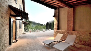 A covered outdoor seating area with two lounge chairs and a brick wall. - Entire Tuscan farmhouse with private pool between Siena and Florence (San Gimignano)