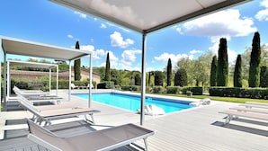 A poolside area with lounge chairs and a covered seating area, overlooking a swimming pool and a landscaped garden. - Entire Tuscan farmhouse with private pool between Siena and Florence (San Gimignano)