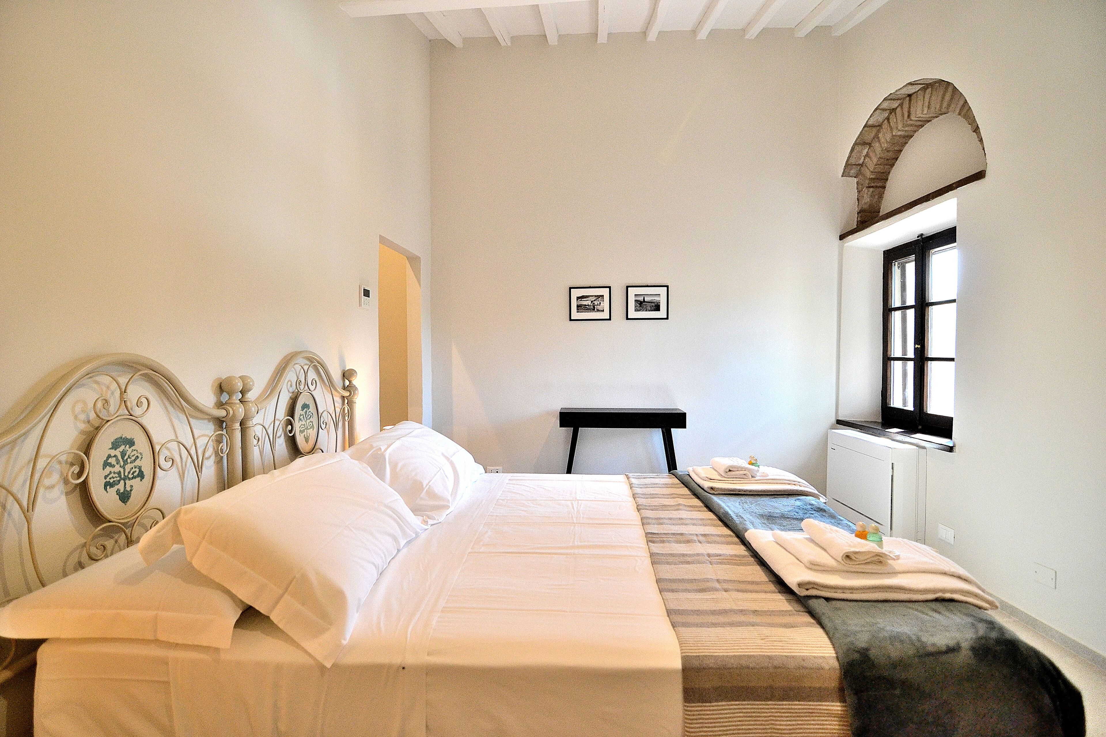Une chambre à coucher avec un lit, une petite table, une fenêtre et deux tableaux encadrés accrochés au mur.