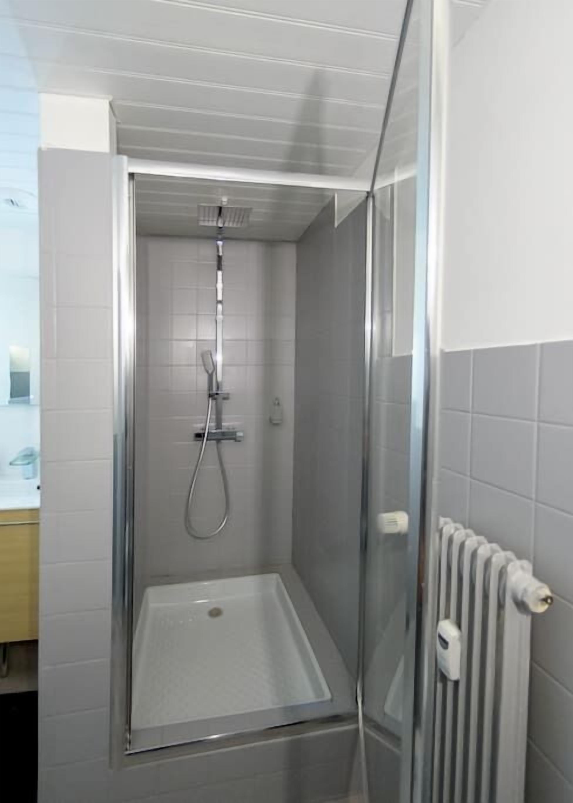 A small, enclosed shower area with a glass door, a showerhead, and a control panel.
